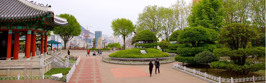 Parque Yongdusan, uma linda vista Coreia do Sul com um pequeno templo, em uma praça com árvores, e prédios de uma cidade grande ao fundo.